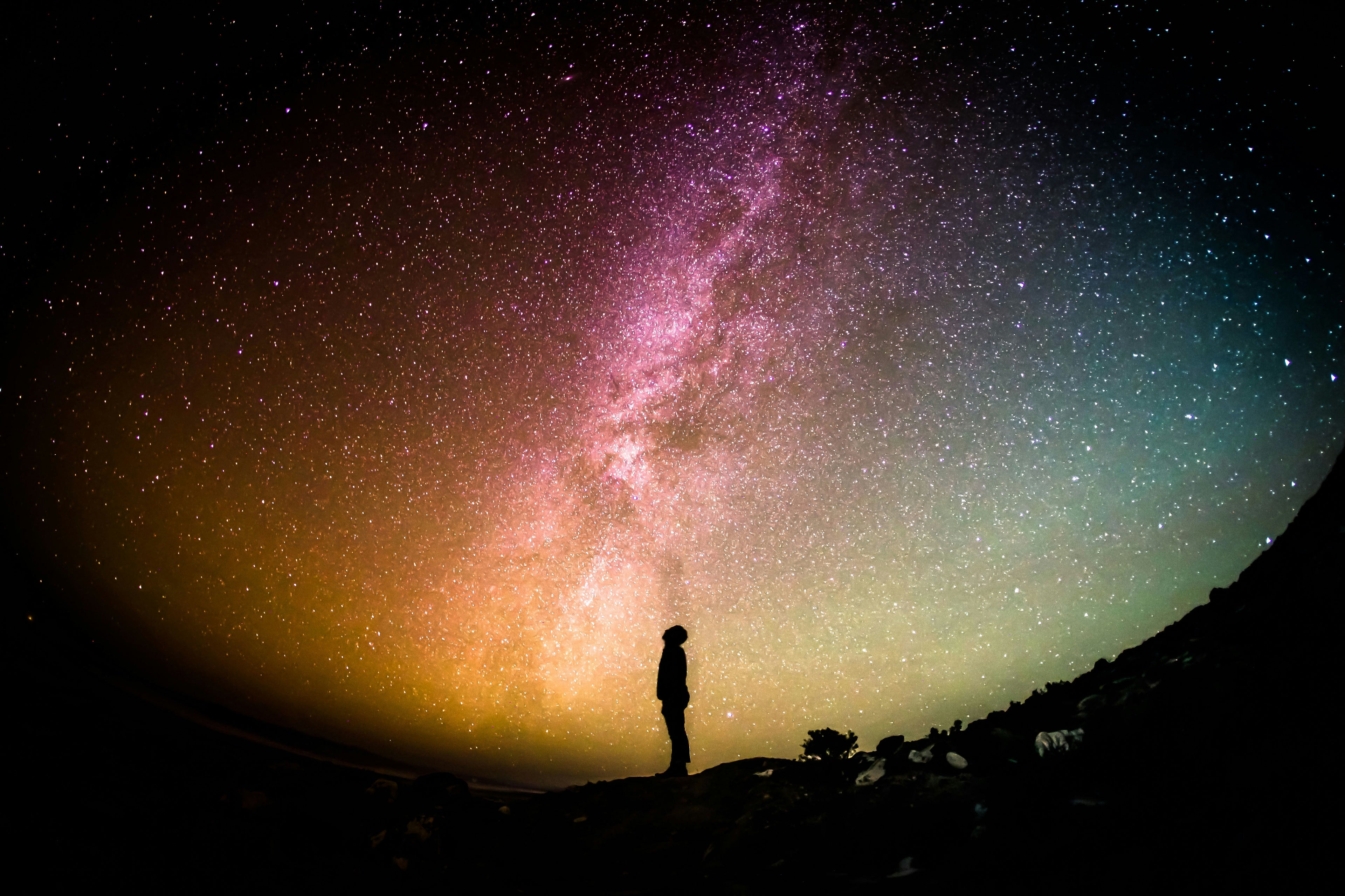 ein Mensch steht vor einem Sternenhimmel in unterschiedlichen Farben. Wissenschaft, Astronomie, Physik, Chemie, Biologie